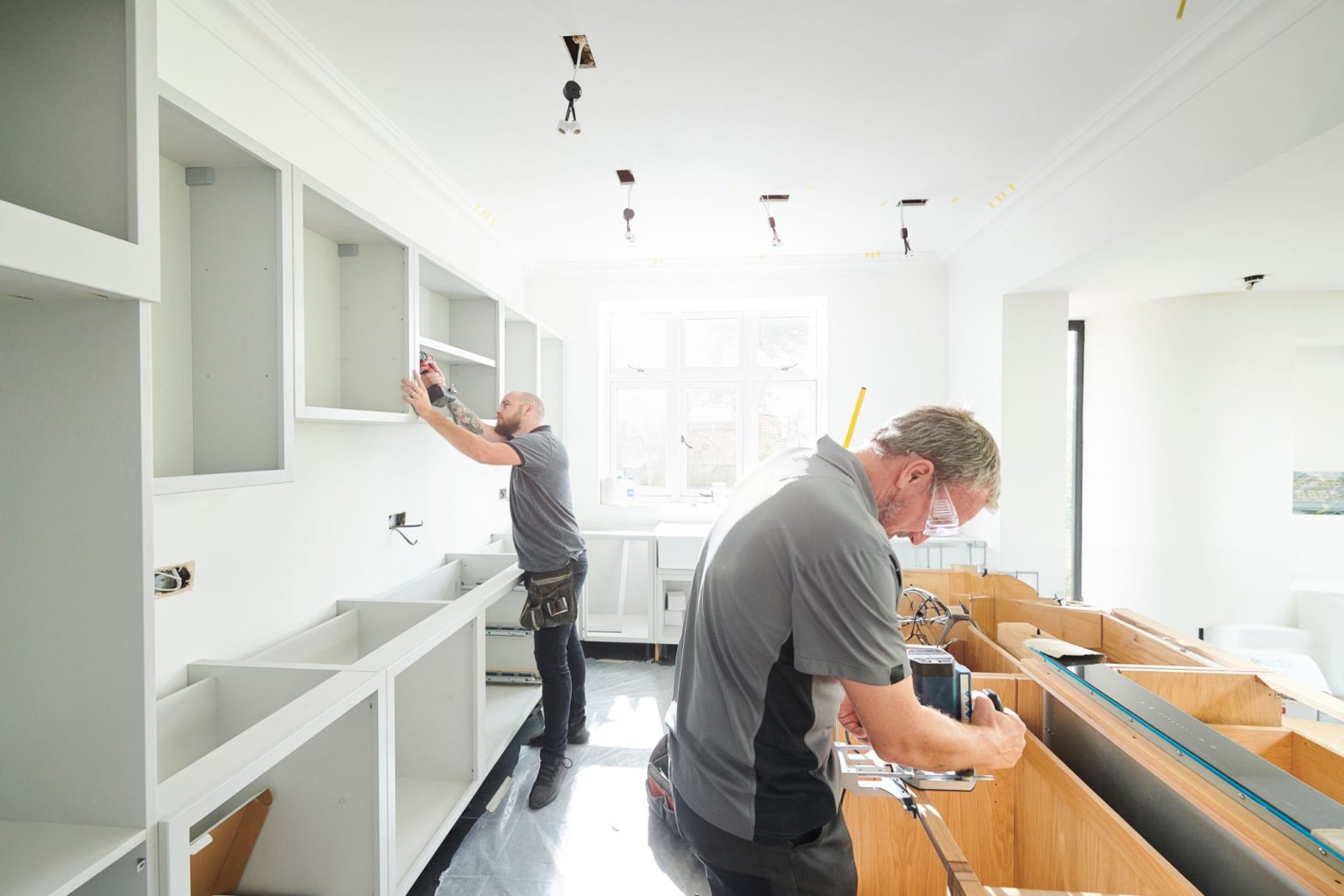 Two men installing white kitchen cabinets -Hire right general contractor